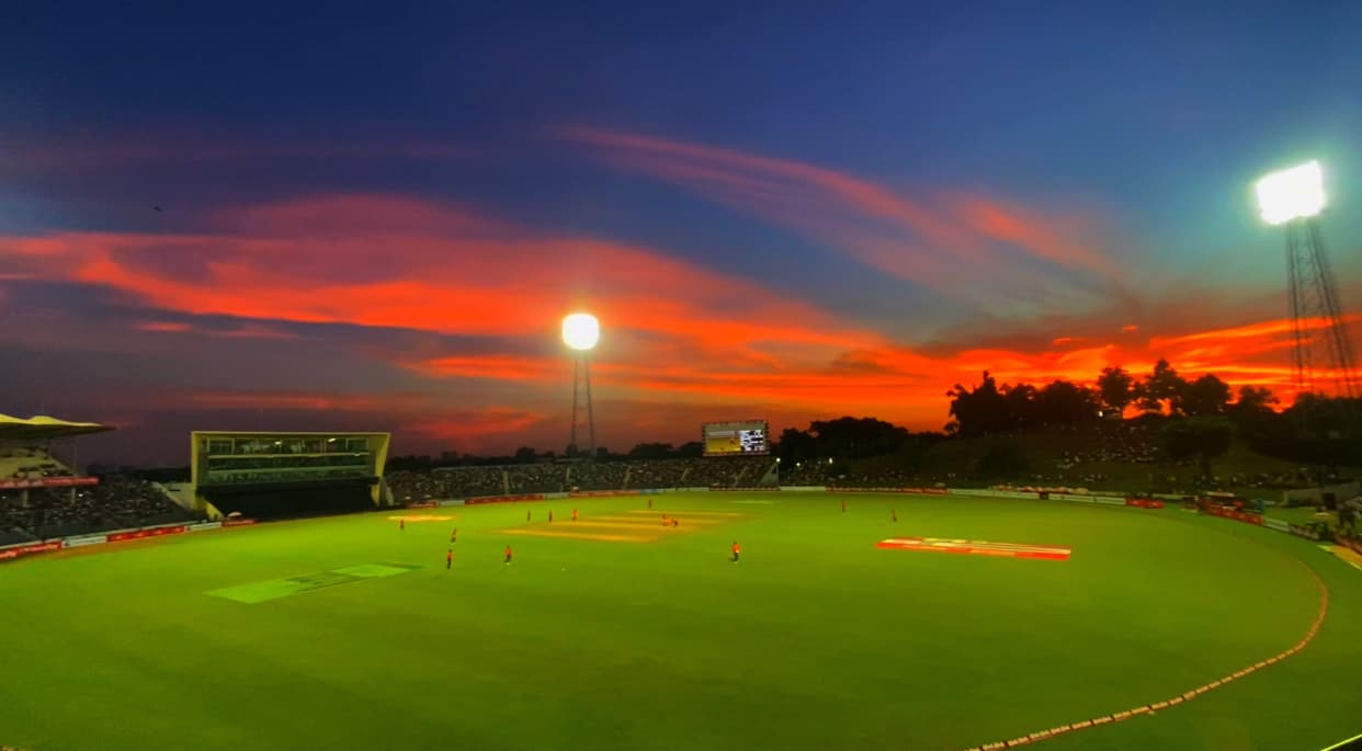 A cricket ground in Sylhet under floodlights, with a red evening sky